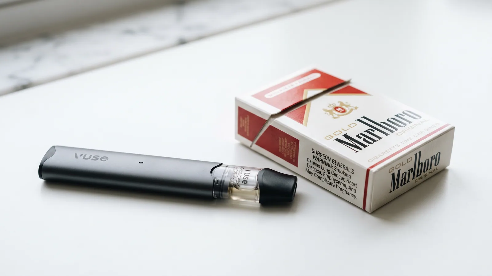 A nicotine vape device next to a pack of cigarettes on a white surface.