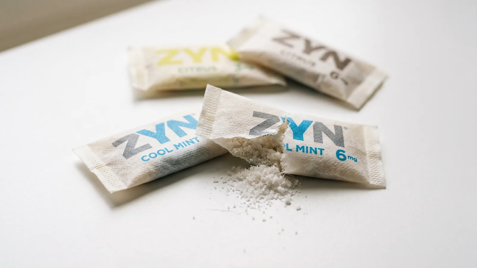 Close-up of nicotine pouches arranged on white surface, one opened to show contents