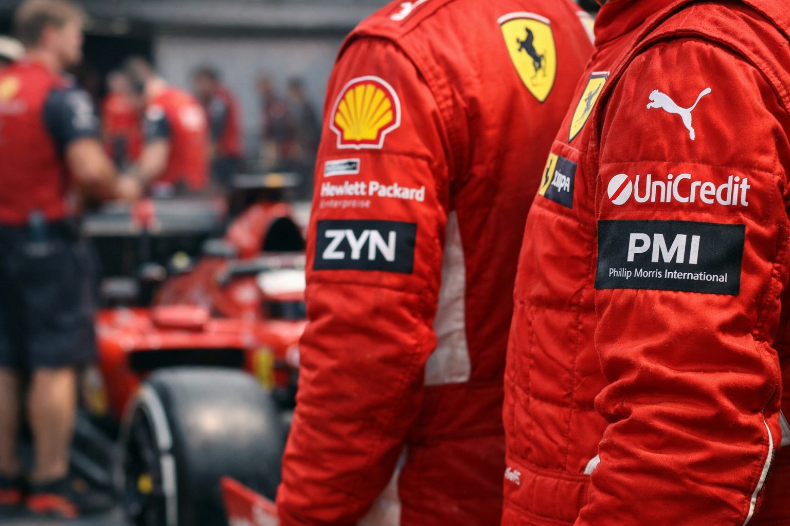 Ferrari Formula 1 paddock scene showing sponsor branding on race suits during a race weekend.